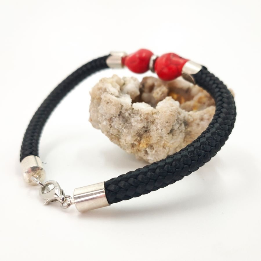 Dubbele schedel en gekruiste botten armband met rode stenen op een dik zwart koord