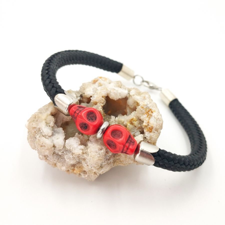 Dubbele schedel en gekruiste botten armband met rode stenen op een dik zwart koord